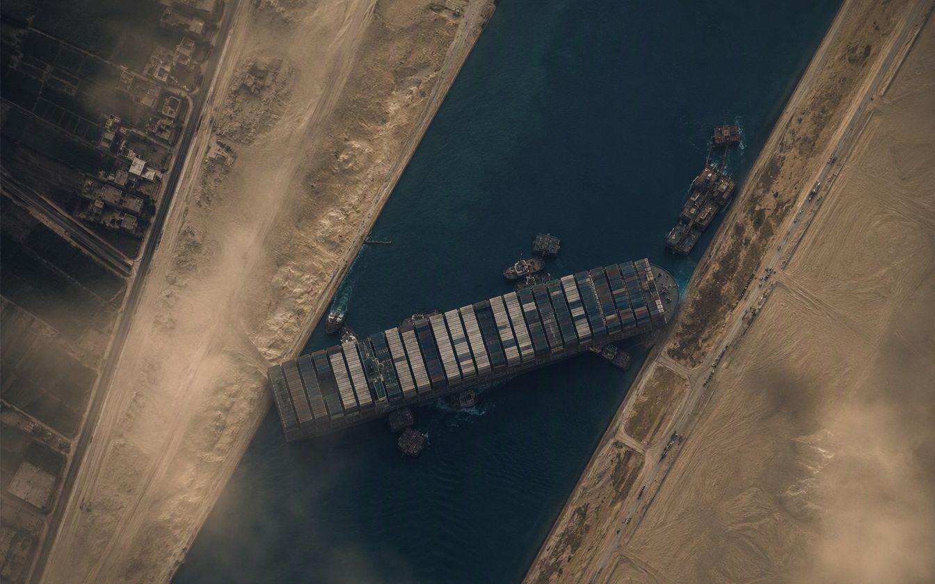 The container ship Ever Given wedged diagonally across the Suez Canal, surrounded by tugboats and dredgers during the March 2021 salvage operation